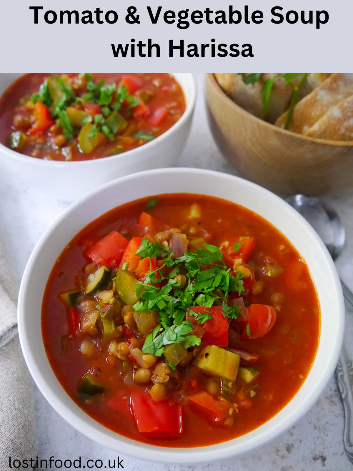 Pinnable image with recipe title and two bowls of tomato and vegetable soup garnished with fresh parsley, with a bowl of sliced crusty bread set alongside.