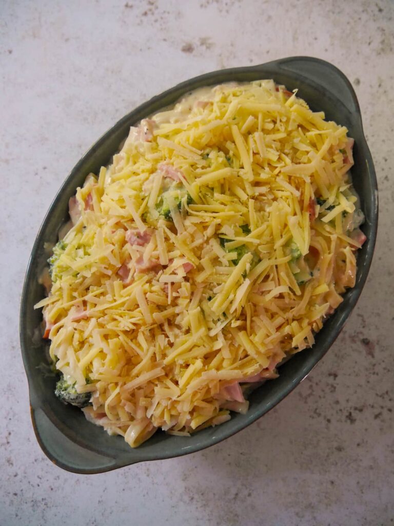 Ham and broccoli pasta bake ingredients in an oven proof dish topped with grated cheese.