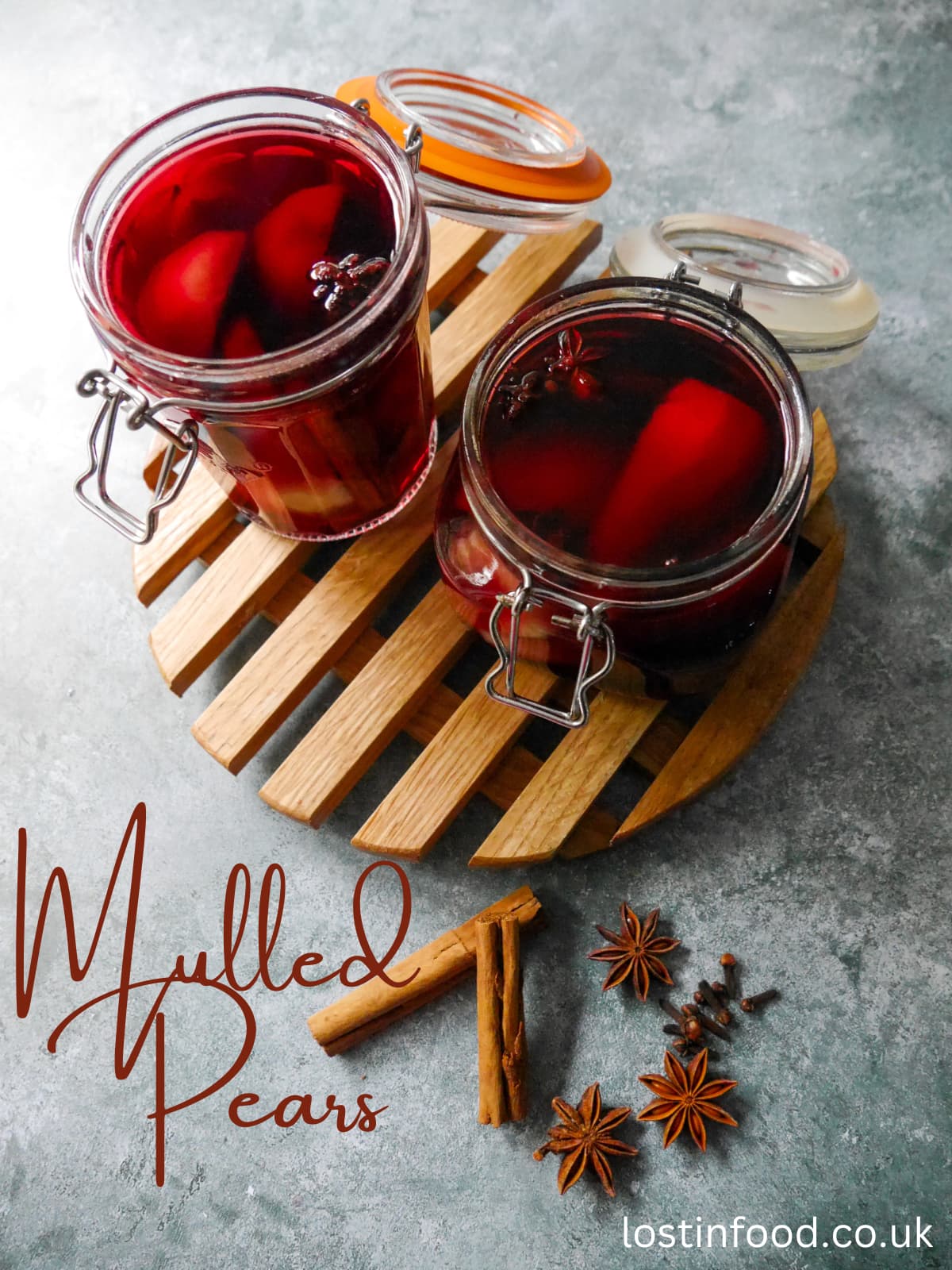 Pinnable image with recipe title and two glass jars filled with pears covered in red wine with whole spices, set on a wooden trivet with whole cloves, star anise and cinnamon sticks set alongside.