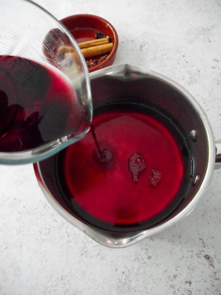 Red wine being poured into a saucepan of sugar syrup.