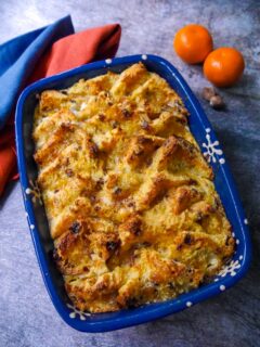 An oven proof dish of panettone bread & butter pudding with two clementines set alongside.