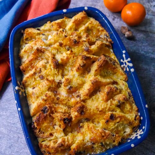 An oven proof dish of panettone bread & butter pudding with two clementines set alongside.