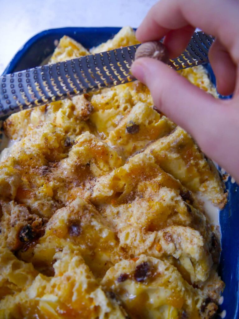 Slices of panettone spread with butter and orange marmalade layered into an oven proof dish with nutmeg being grated over top.