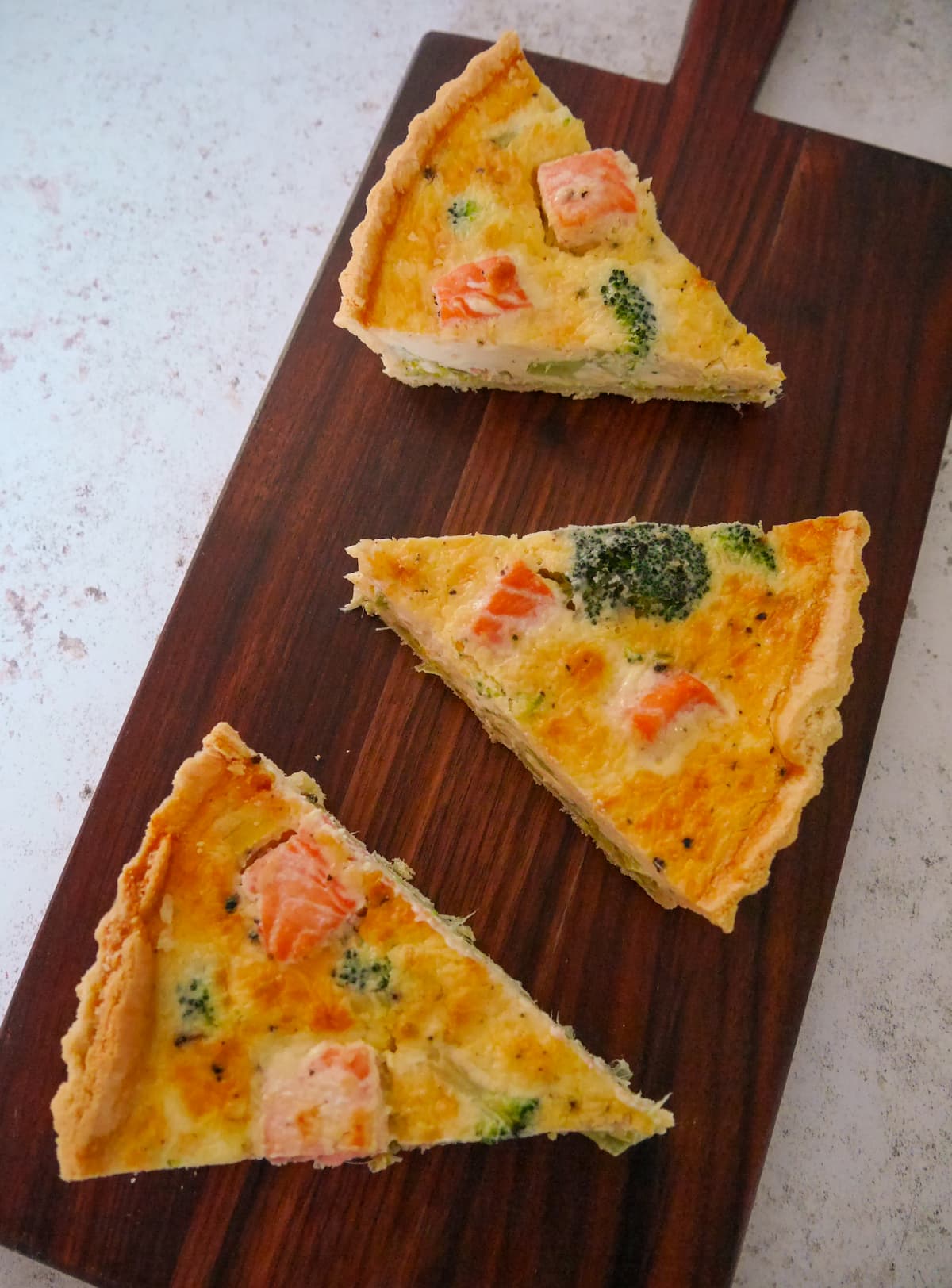 Three wedges of salmon and broccoli tart set on a wooden platter.