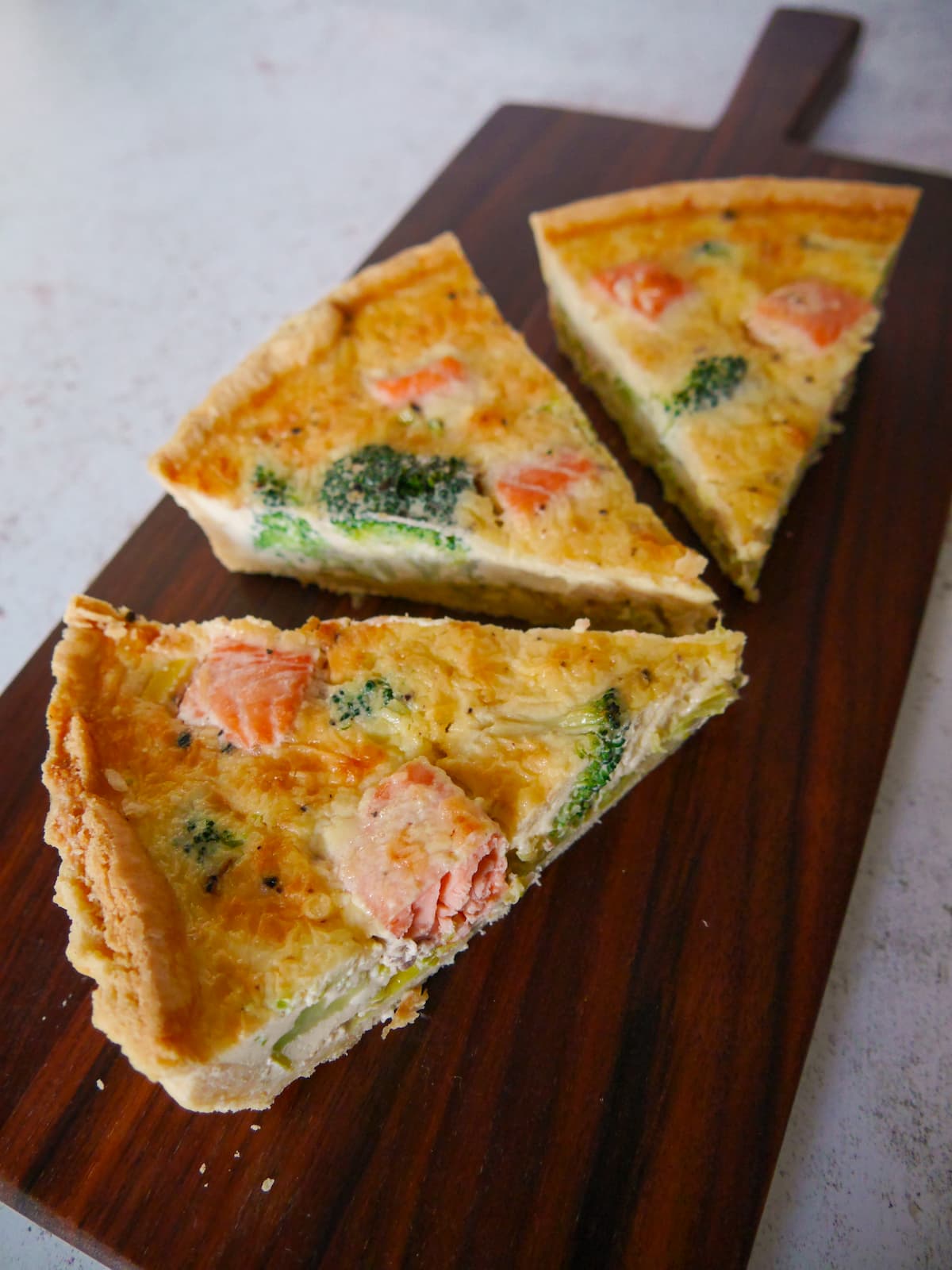 Three wedges of salmon and broccoli tart set on a wooden platter.