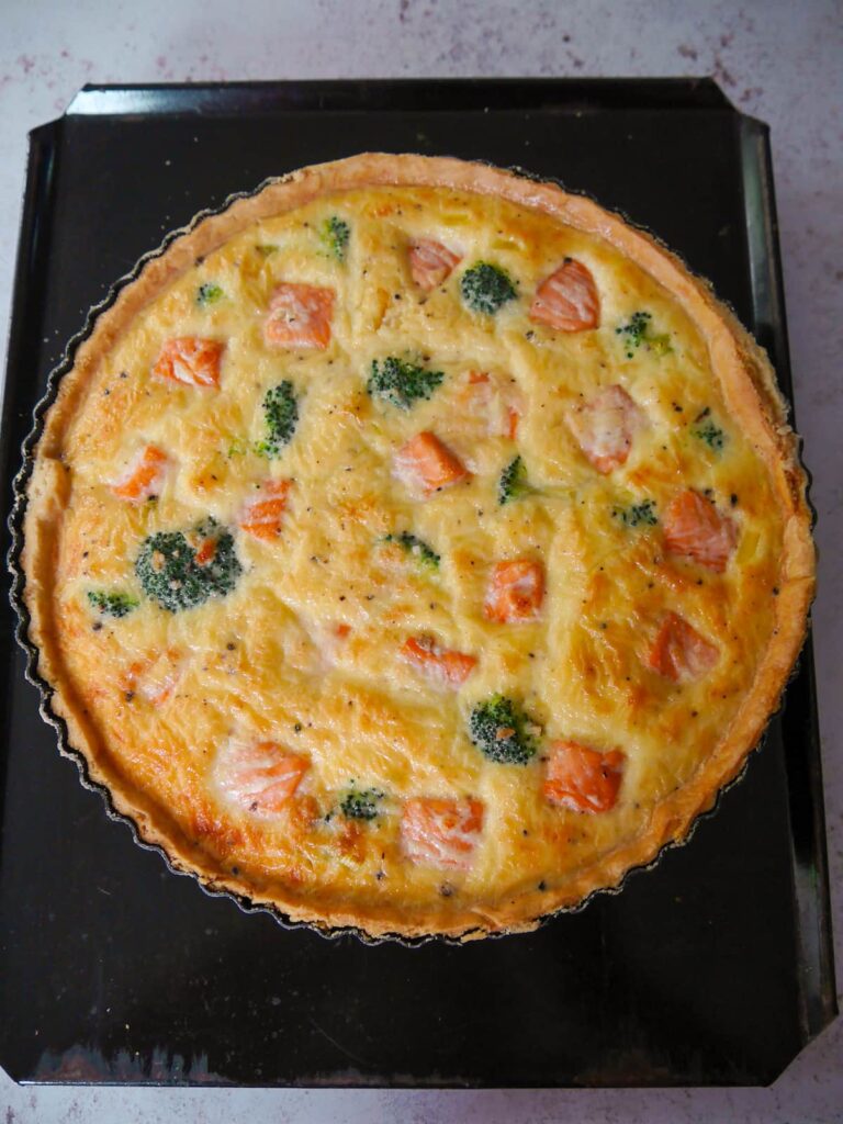 Freshly based salmon tart with broccoli on a baking sheet.