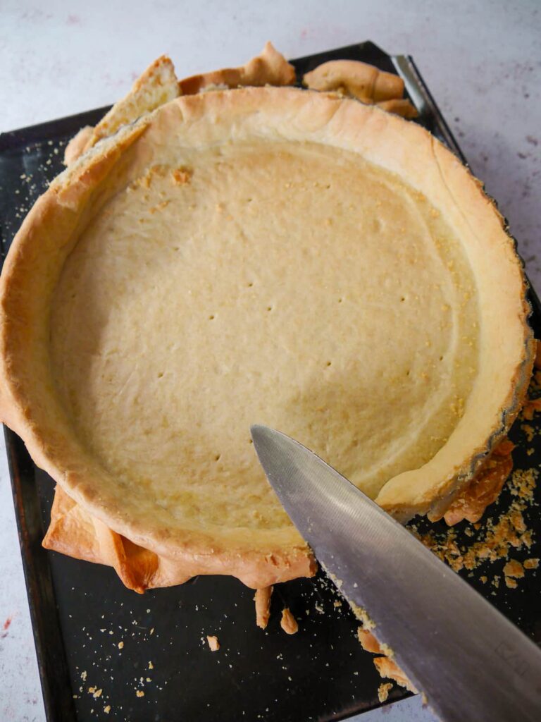 A part baked pastry case being trimmed with a sharp knife.