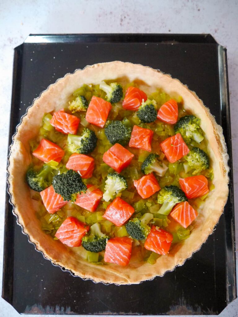 Part baked pastry tin with a layer of sauteed leeks, topped with chunks of raw salmon and par-cooked broccoli florets.