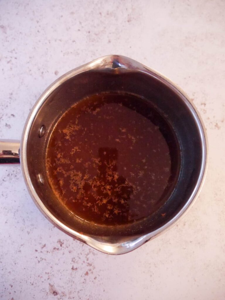 A saucepan filled with melted coconut oil, honey, vanilla extract, spices and salt.