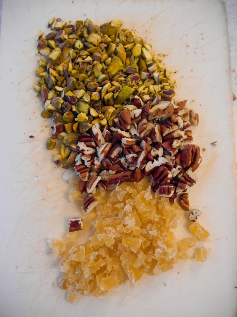 A chopping board topped with chopped pistachios, pecans and crystallised ginger