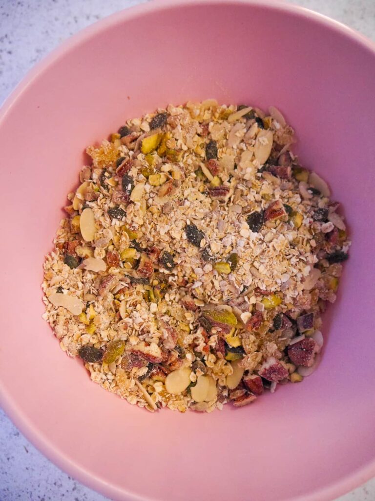 A pink bowl filled with porridge oats, chopped nuts, seeds and crystallised ginger.