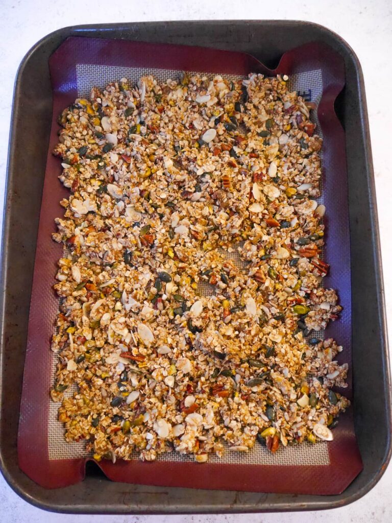 A large roasting tin, lined with a silicone mat, with Granola mix spread evenly over.