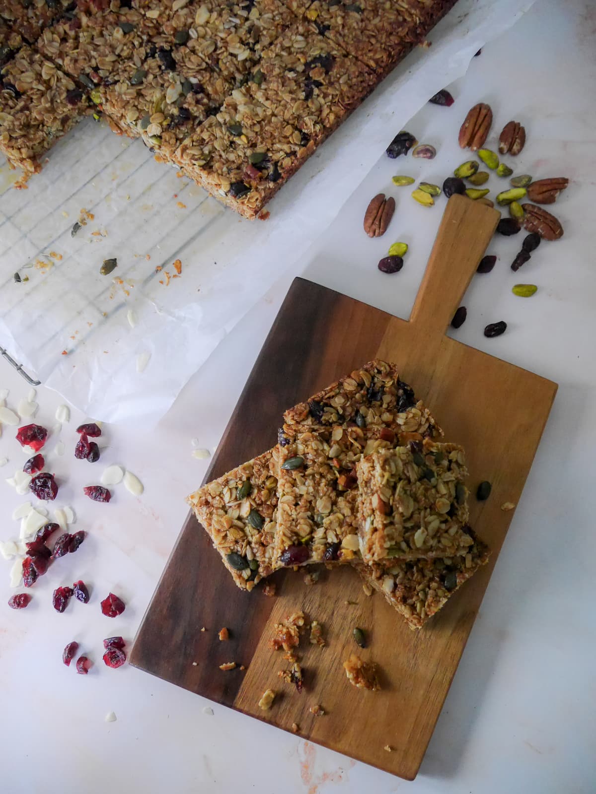 A wooden board topped with 5 slices of Christmas spiced flapjacks with a wire tray of cut flapjacks set alongside.