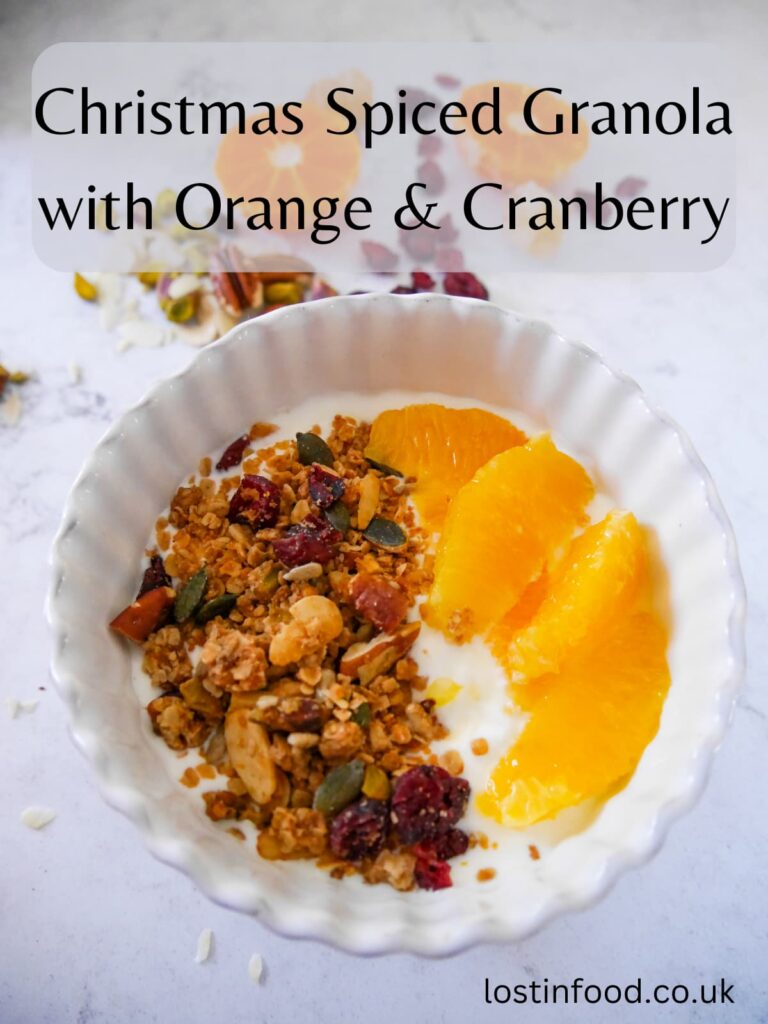 Pinnable image with recipe title and a white bowl filled with Greek yogurt topped with slices of fresh orange and Christmas spiced granola with orange and cranberries.