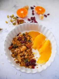 A white bowl filled with Greek yogurt topped with slices of fresh orange and Christmas spiced granola with orange and cranberries.