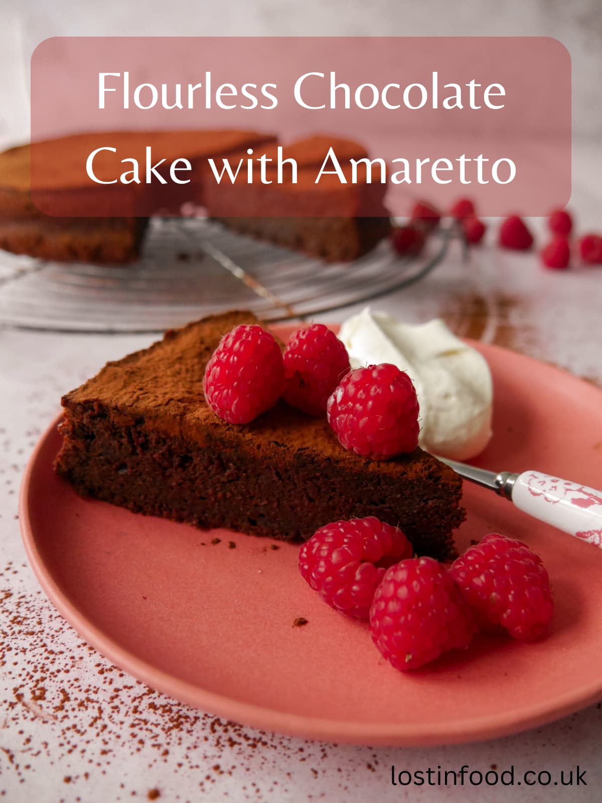 A pinnable image with recipe title, and flourless chocolate cake with amaretto sliced and set on a wire rack, with a pink plate with a slice of flourless chocolate amaretto cake topped with fresh raspberries and served with whipped cream set alongside.