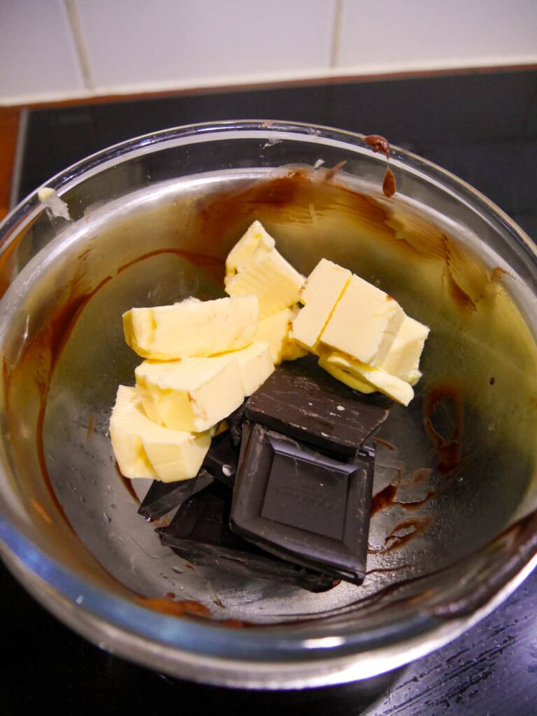 A glass bowl filled with cubed butter and broken dark chocolate set over a pan of boiling water.