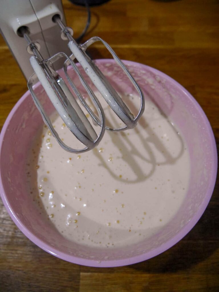 A pink mixing bowl of whisked egg and sugar.