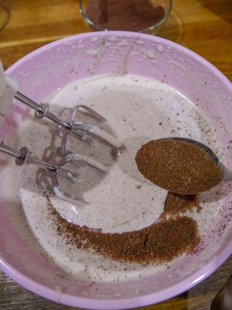 Ground almond and cocoa powder mixture being added a spoon at a time to whisked egg and sugar mixture.