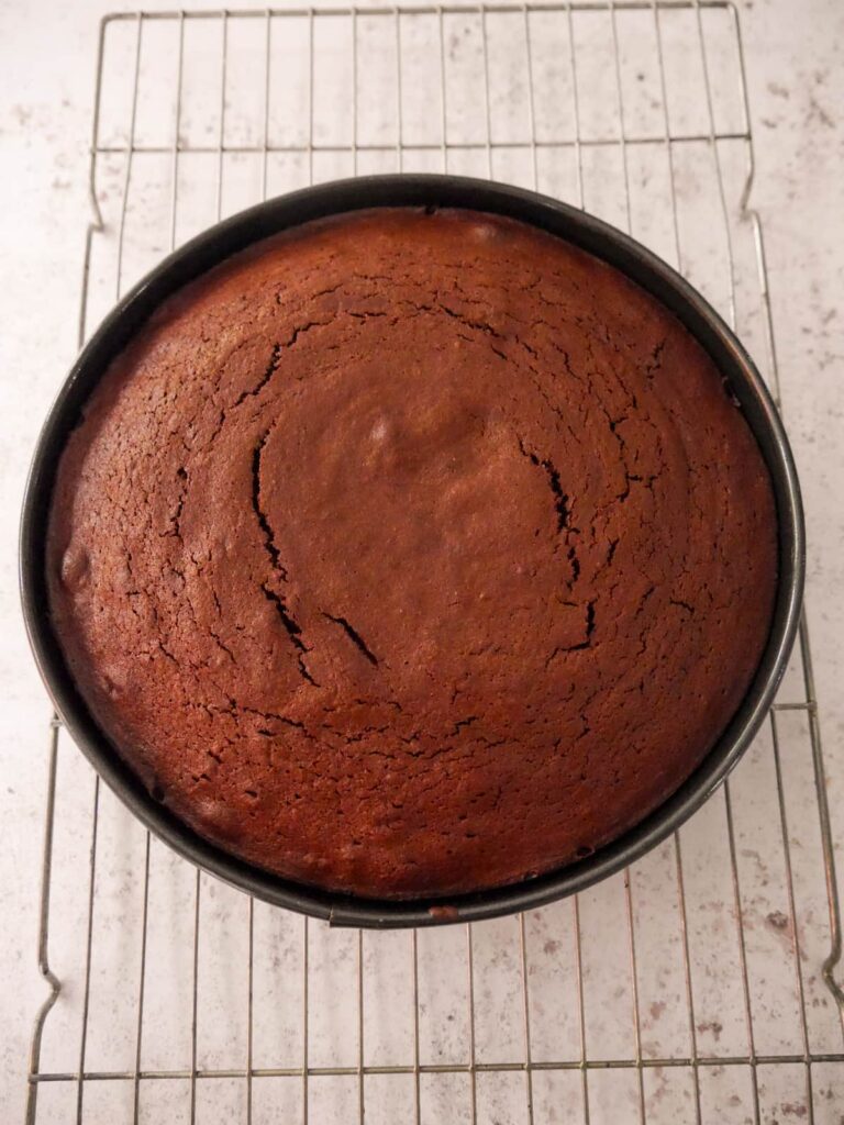 A round baking tin with baked flourless chocolate cake set on a wire cooling rack.