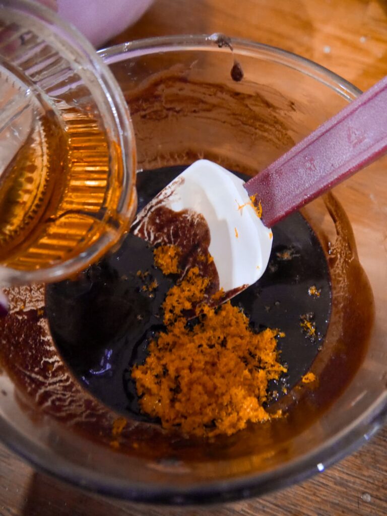 A glass bowl filled with melted dark chocolate and butter with added orange zest and orange liqueur.