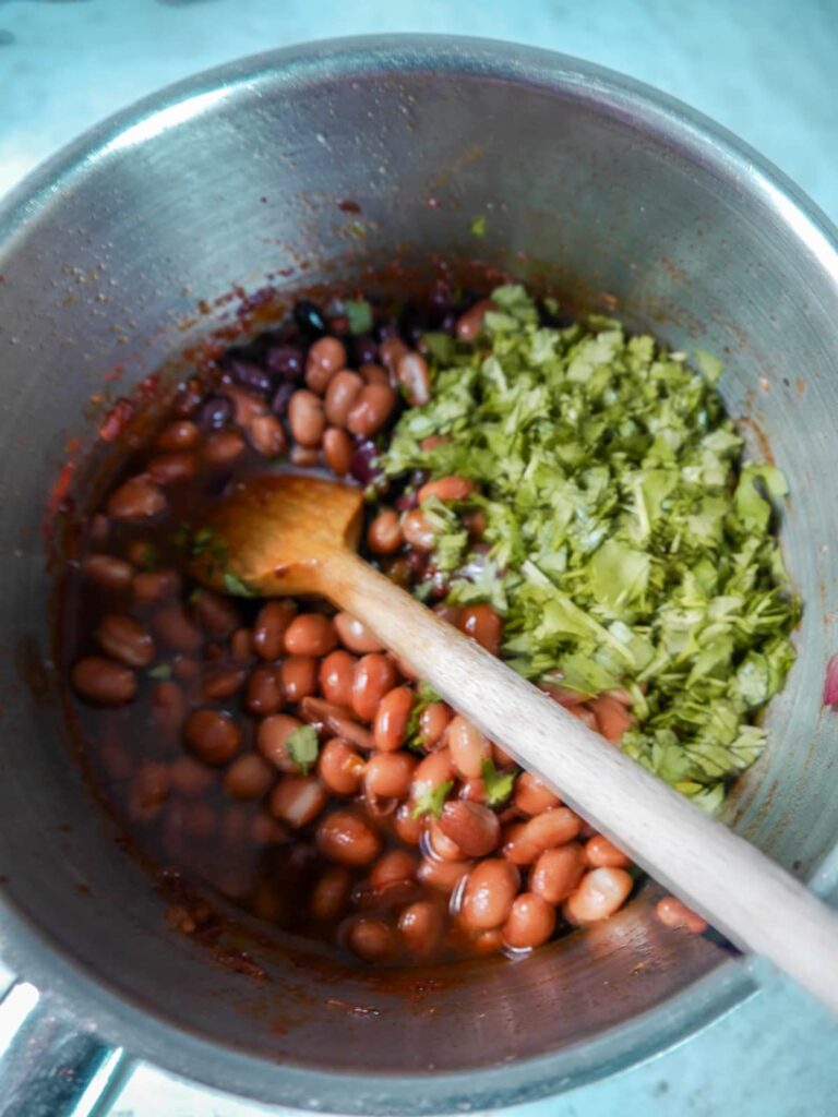 A saucepan filled with vegetables, canned beans and chopped coriander.
