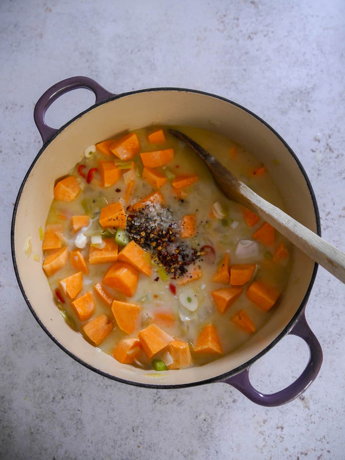 A Dutch oven filled with sauteed vegetables with added sweet potato, seasoning, coconut milk and stock.