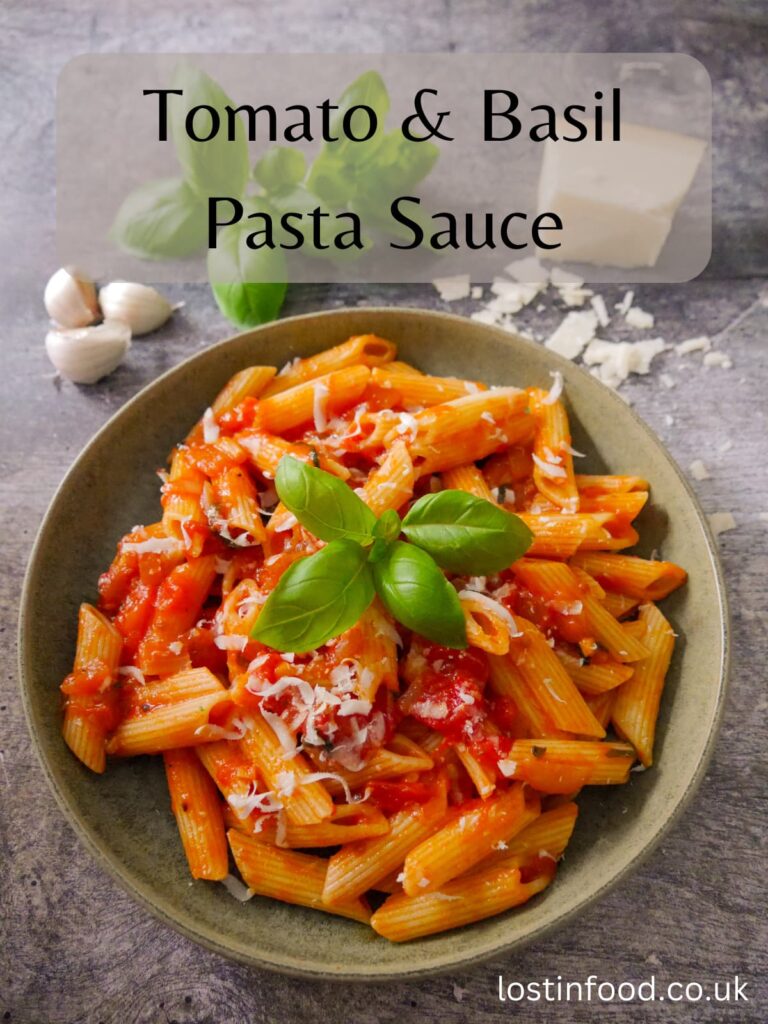Pinnable image with recipe title and green bowl filled with penne pasta in a tomato, basil pasta sauce with a garnish of parmesan cheese and fresh basil leaves, with a block of parmesan, fresh basil leaves and garlic set alongside.