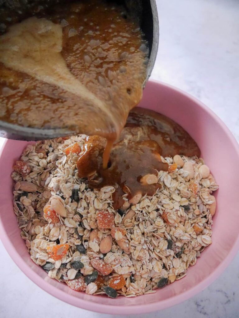 A large mixing bowl filled with dry flapjack mixture, with honey and melted butter mixture being poured over.