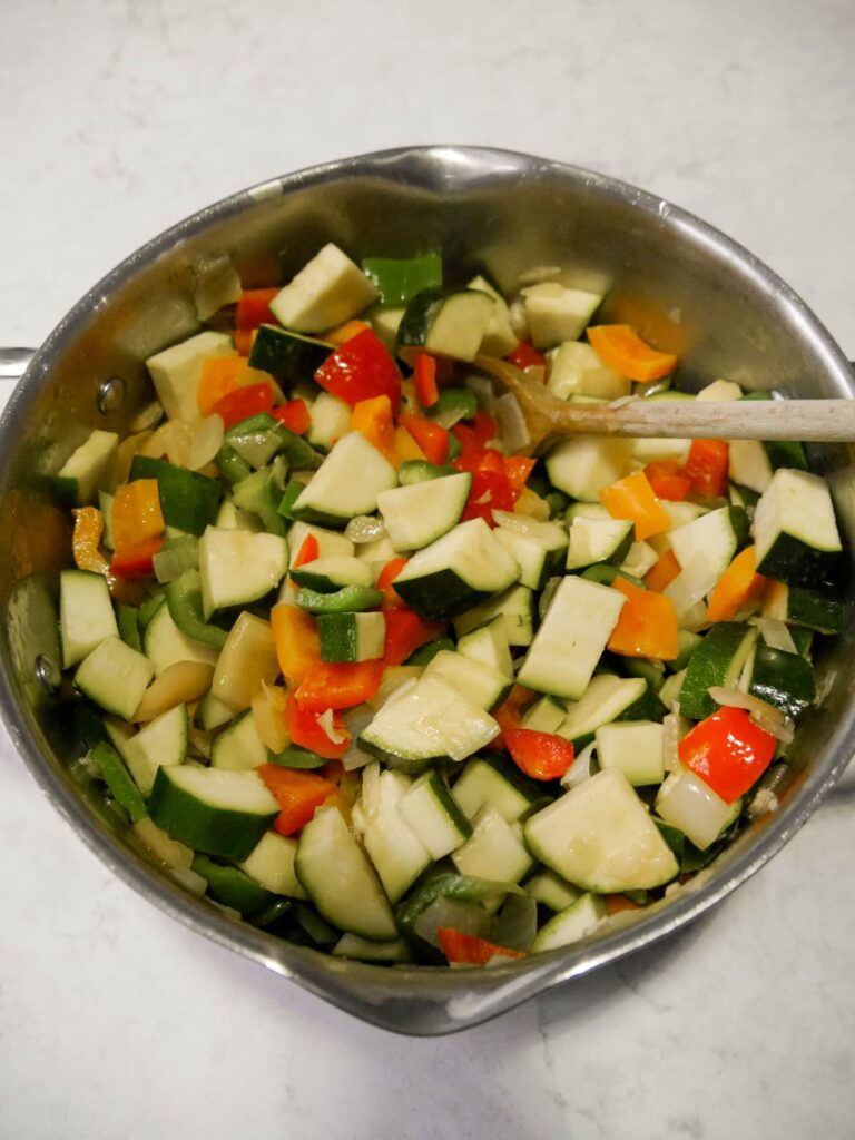 A pan filled with sauteed chopped onion, red, green and yellow peppers and courgettes.