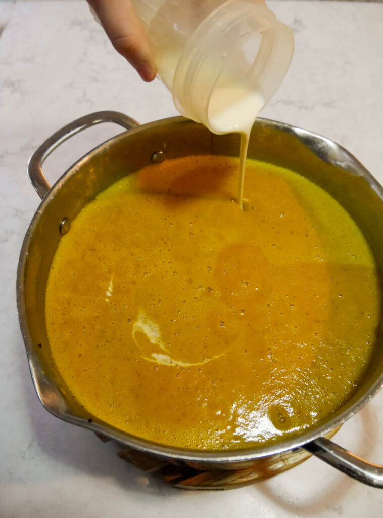 Blended courgette and pepper soup with cream being added to the pan.