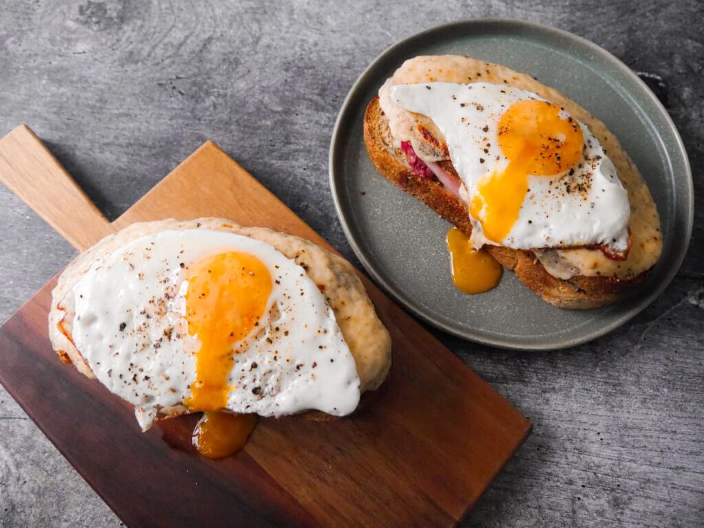Two plates topped with toasted croque madame toasted sandwiches topped with a fried egg.