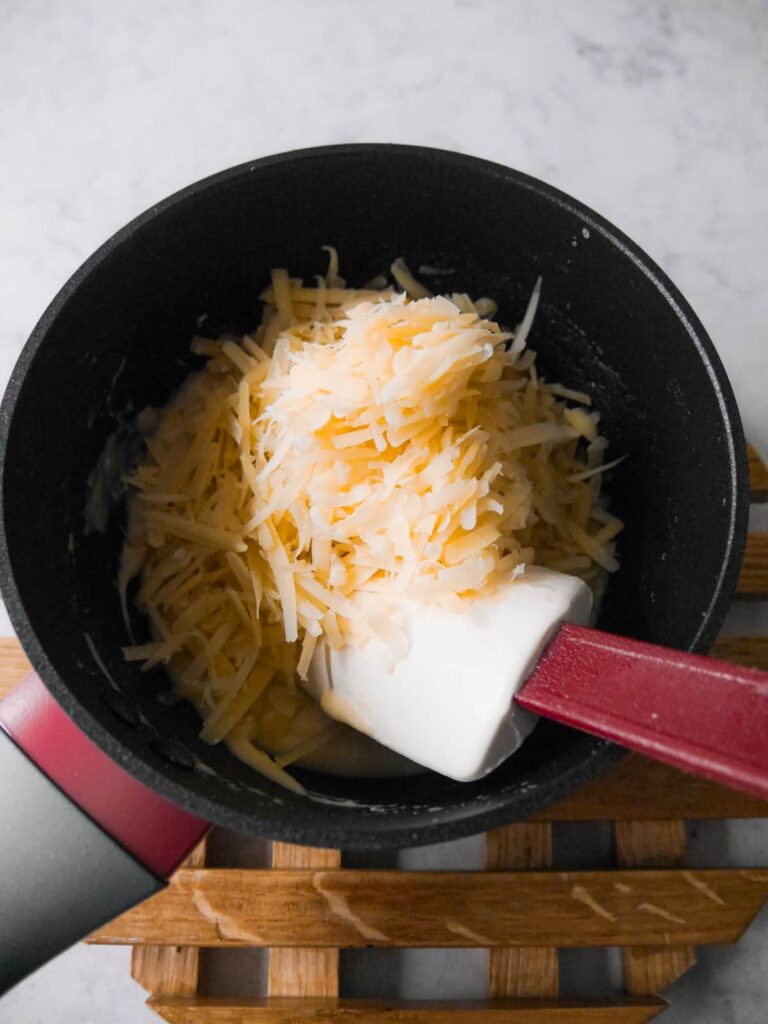 Grated cheese being added to a saucepan of bechamel sauce.