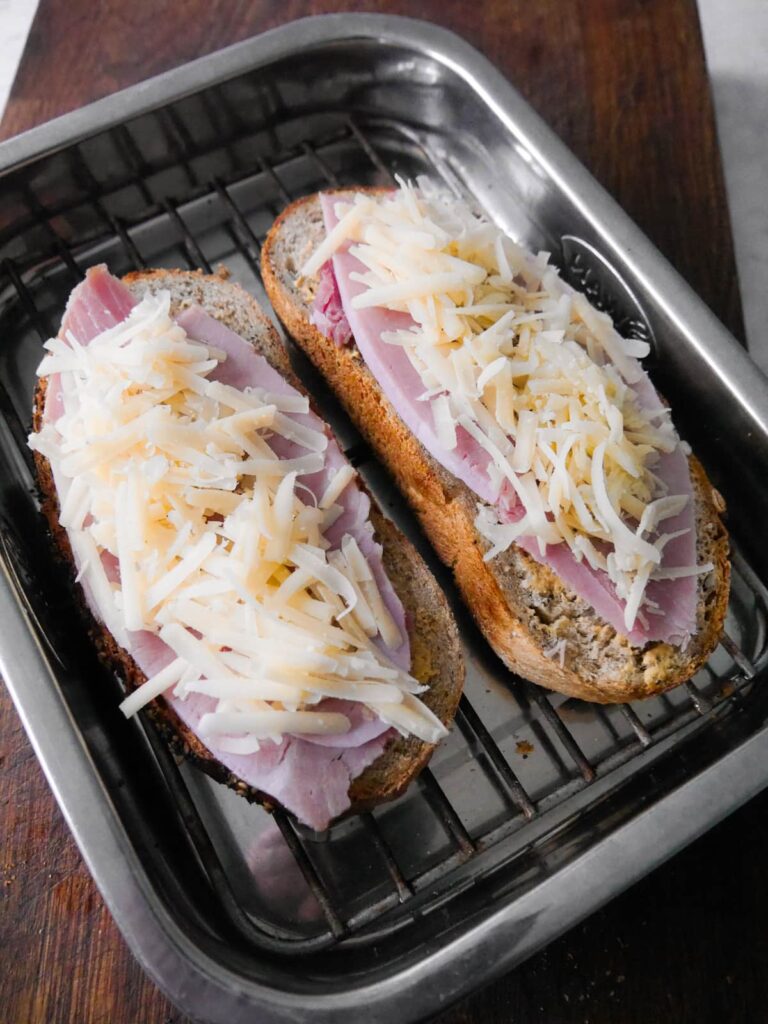 Two slices of bread topped with sliced ham and grated cheese.