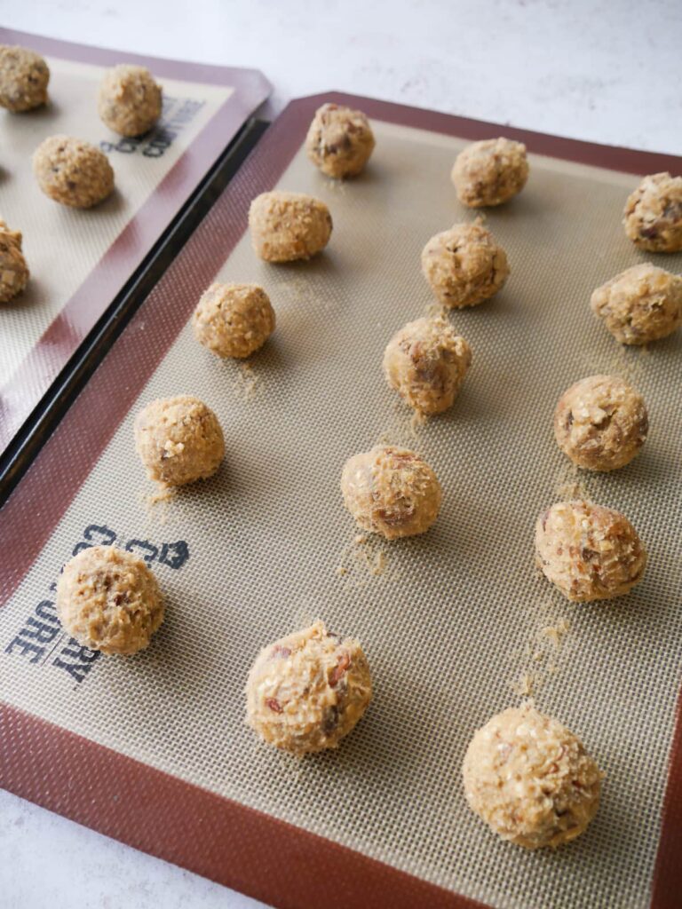 A silicone mat lined baking sheet topped with golf ball sized balls of date oat cookie dough.