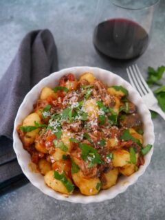 A bowl of Italian beef ragu, served with gnocchi and garnished with fresh parsley and grated parmesan cheese.