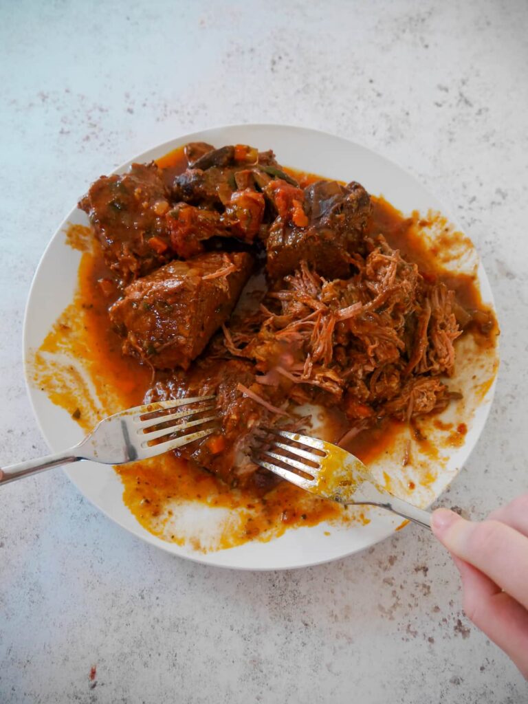 A plate of cooked chunks of beef brisket being pulled apart with 2 forks.