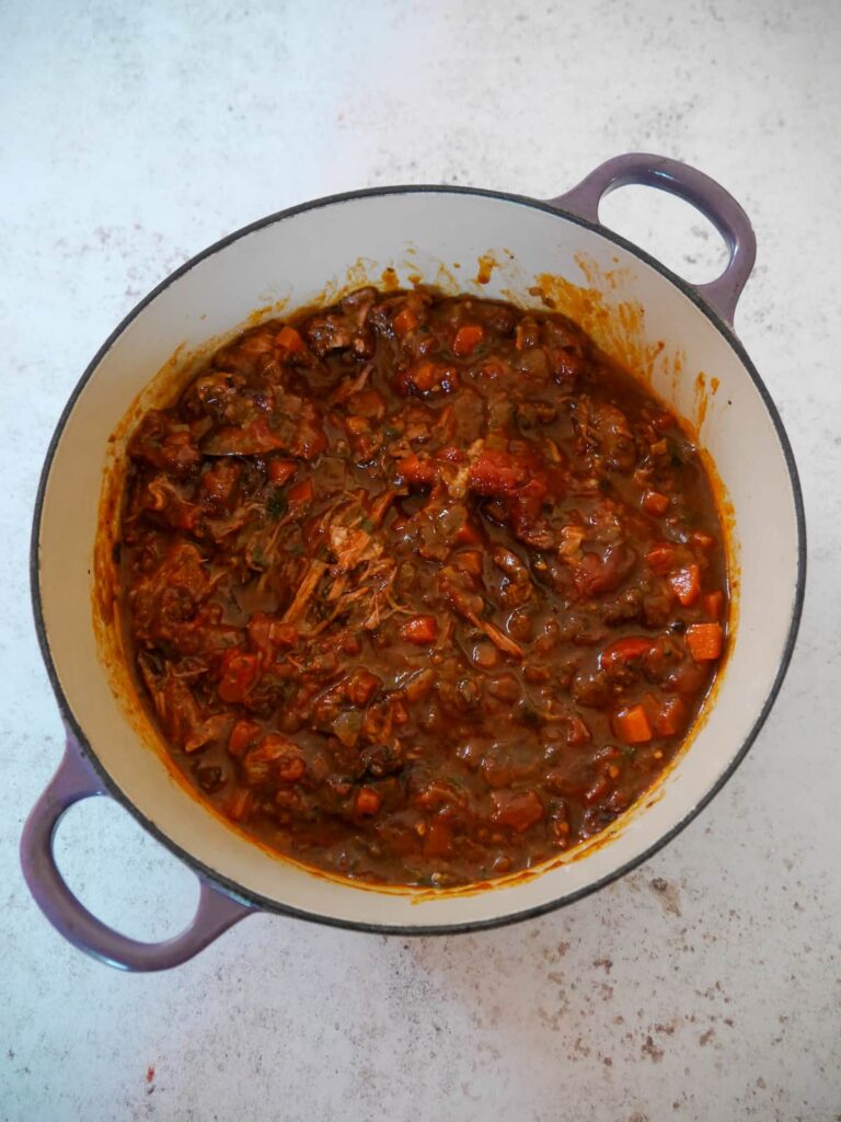 A Dutch oven filled with cooked and shredded beef brisket in an Italian beef ragu sauce.