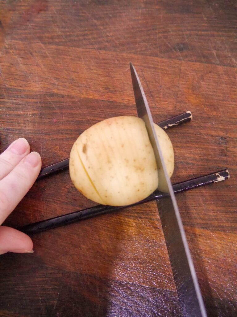 New Potato set over two parallel chopsticks with sharp knife slicing part way through the potato.