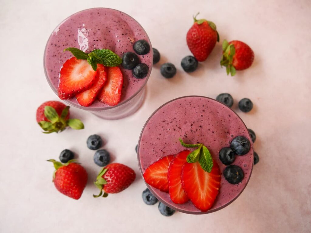 Two glasses of strawberry & blueberry smoothie garnished with fresh blueberries and strawberry slices.