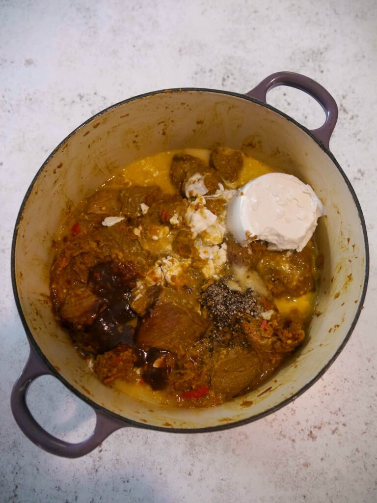 A Dutch oven filled with sauteed spice vegetables and beef chunks, with added coconut milk, tamarind paste and beef stockpot.