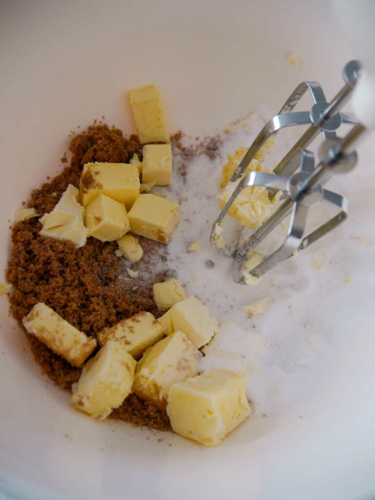 A bowl of brown sugar, caster sugar and butter being whipped together using an electric hand whisk.