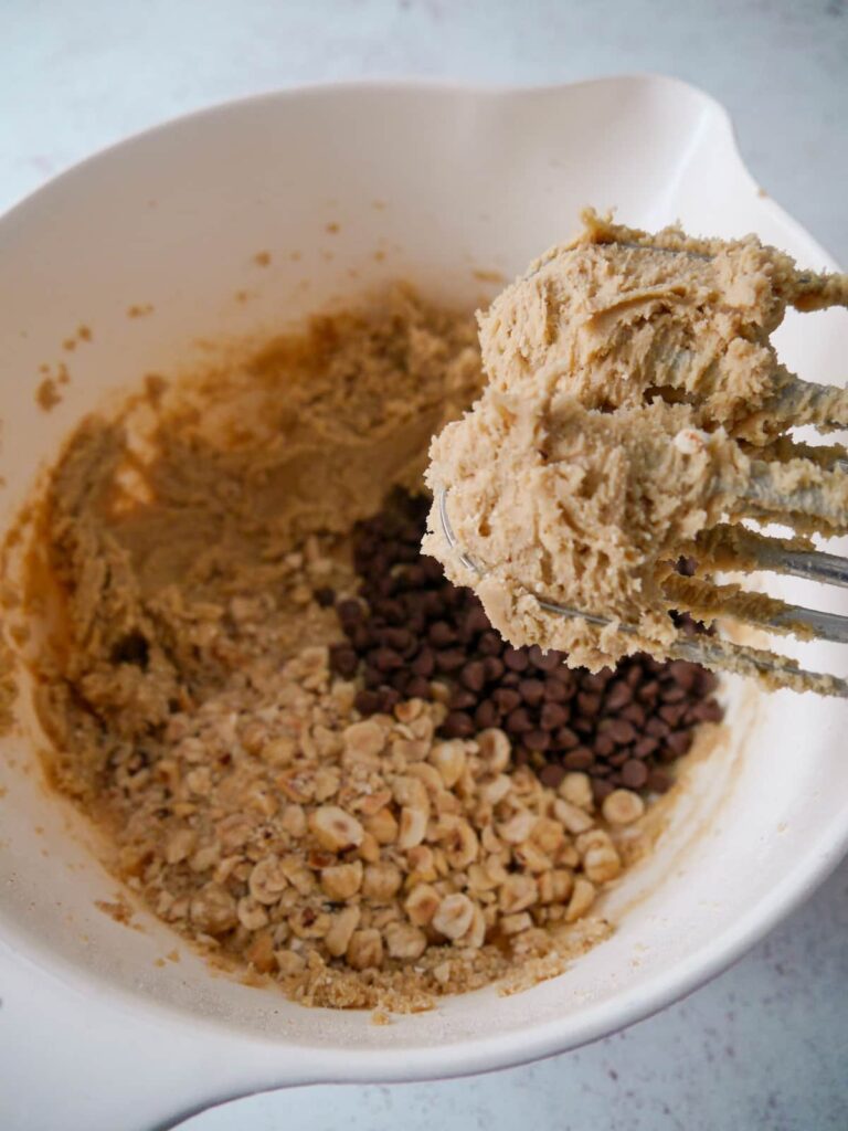 A bowl of cookie dough with added chocolate chips and crushed hazelnuts.