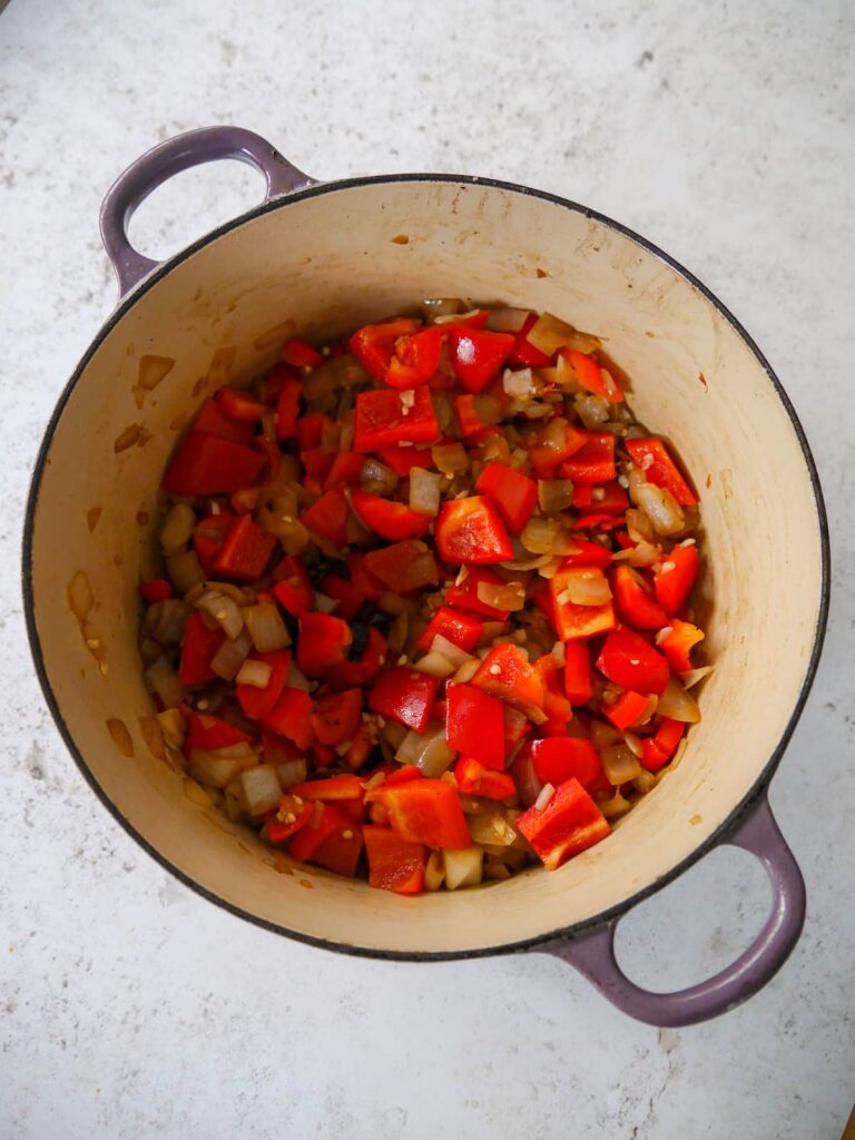 A Dutch oven filled with sauteed onion, garlic, red pepper and red chilli.
