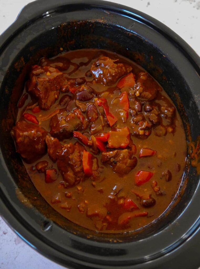 A slow cooker filled with cooked chunky beef chilli.