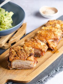 Portions of roasted pork belly with crispy crackling top set out on a wooden board.