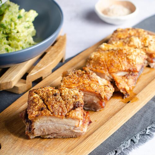 Portions of roasted pork belly with crispy crackling top set out on a wooden board.