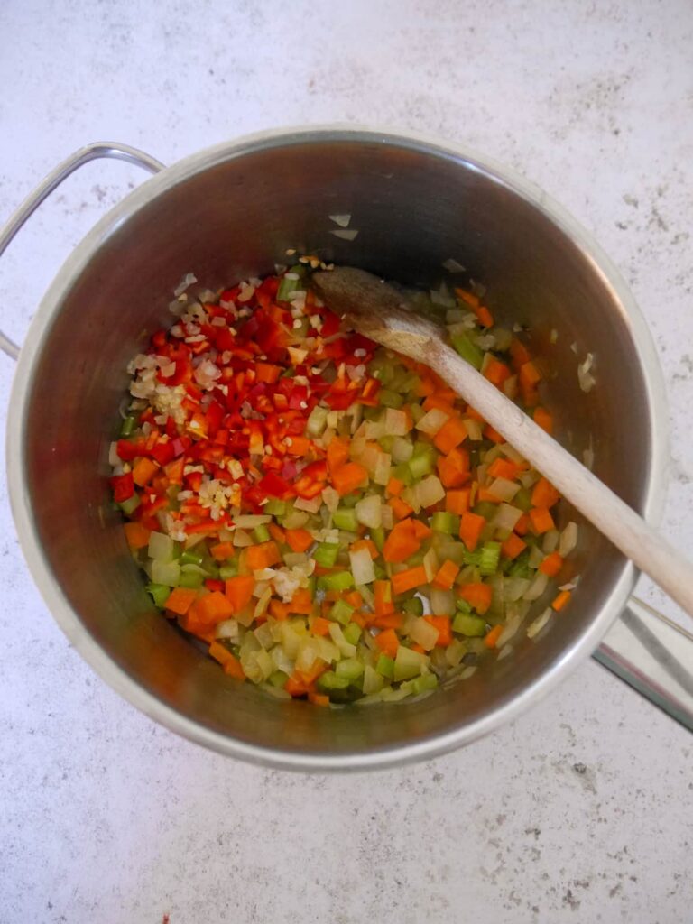 A large saucepan filled with sauteed carrots, celery, onion, garlic and red chilli.