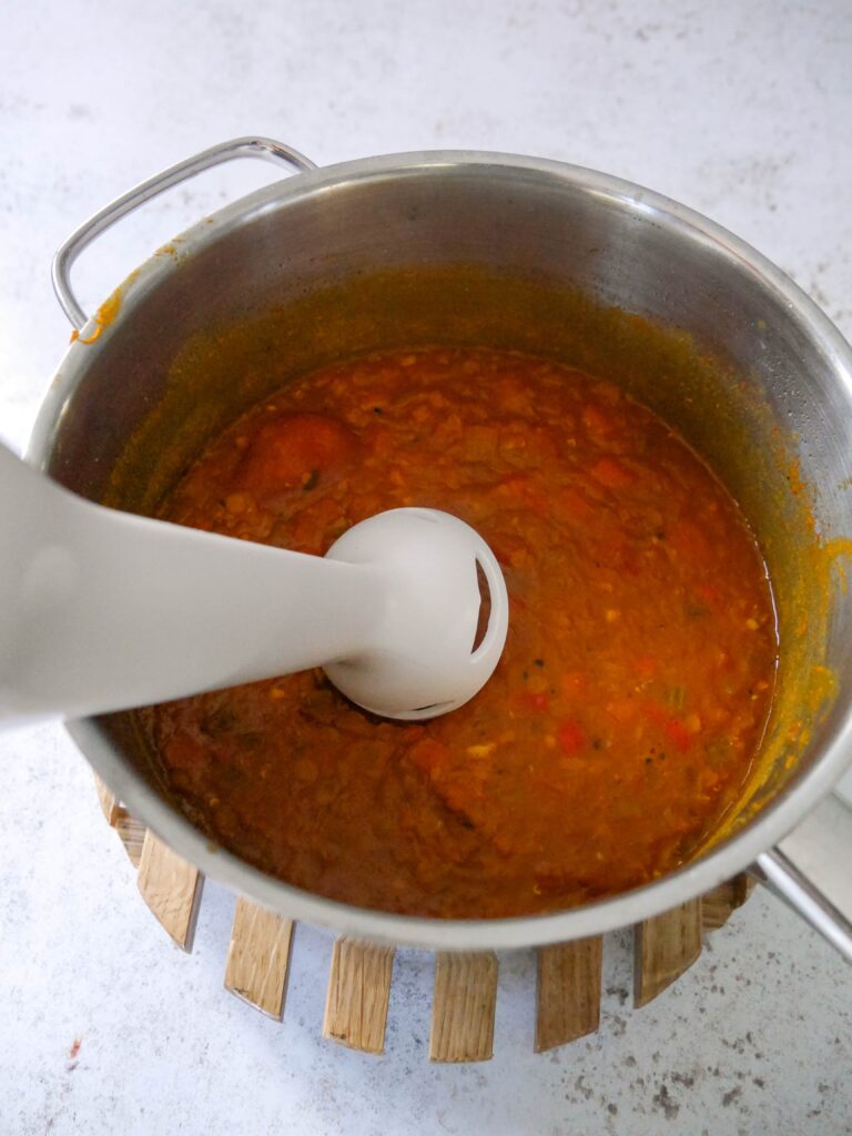 A large saucepan of spicy lentil soup being blitzed with an immersion blender.