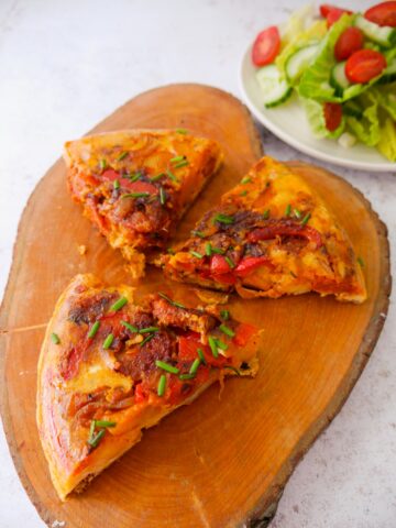3 slices of Spanish Chorizo tortilla set on a wooden board with a salad set alongside.